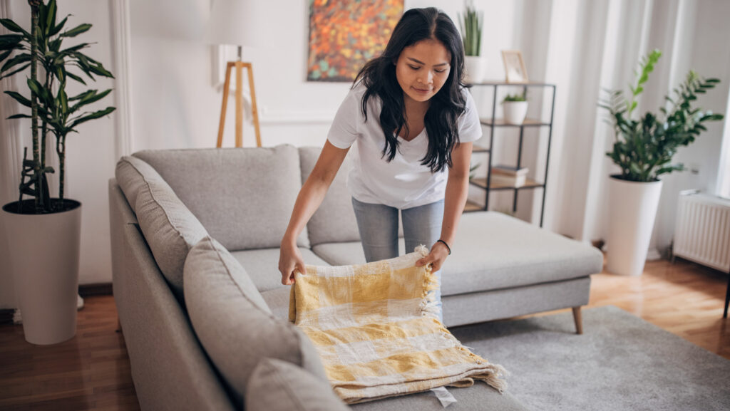 One woman, beautiful Asian woman standing in living room at home. She is folding a blanket.